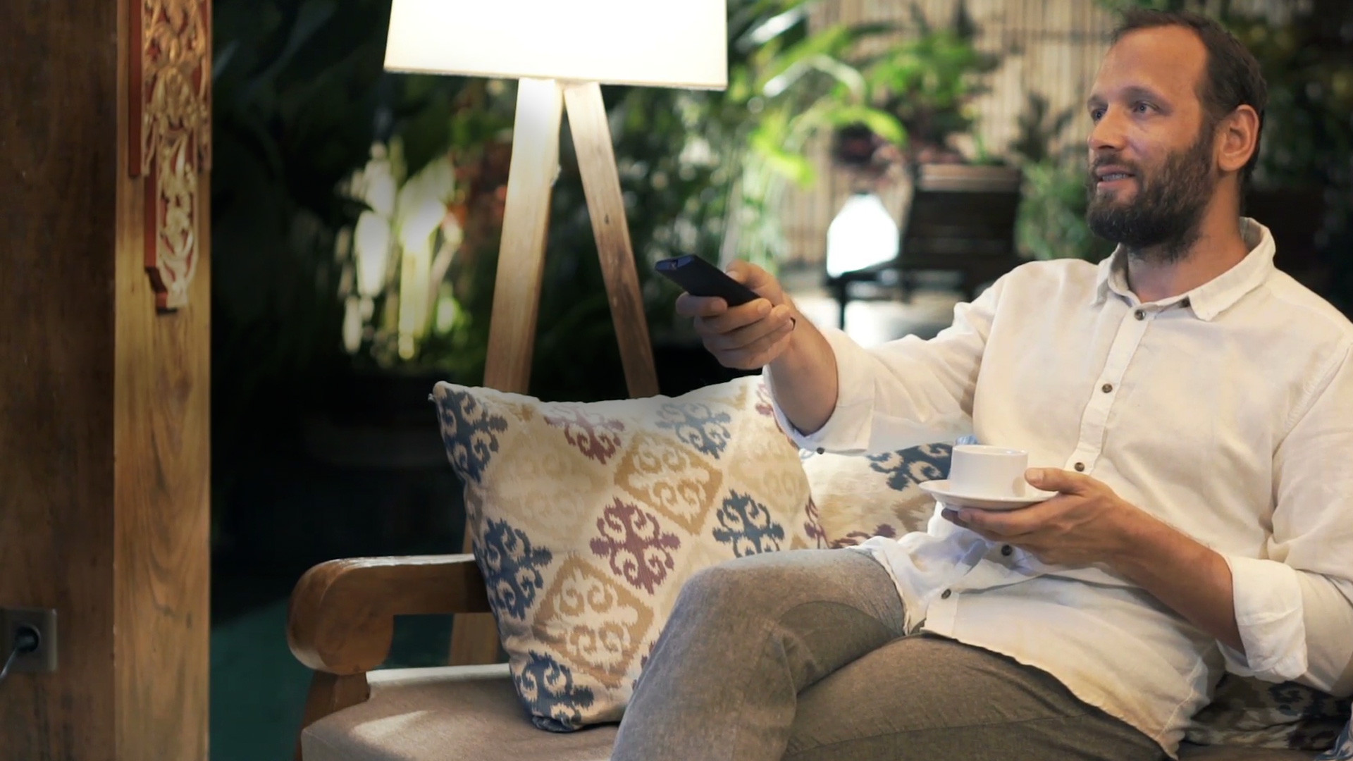 Man sitting on sofa with coffee cup and remote control. Man sitter i soffa med kaffekopp och fjärrkontroll.
