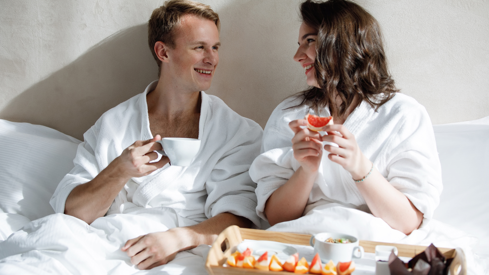 A couple having breakfast in a hotel bed. Ett par som äter frukost i en hotellsäng.