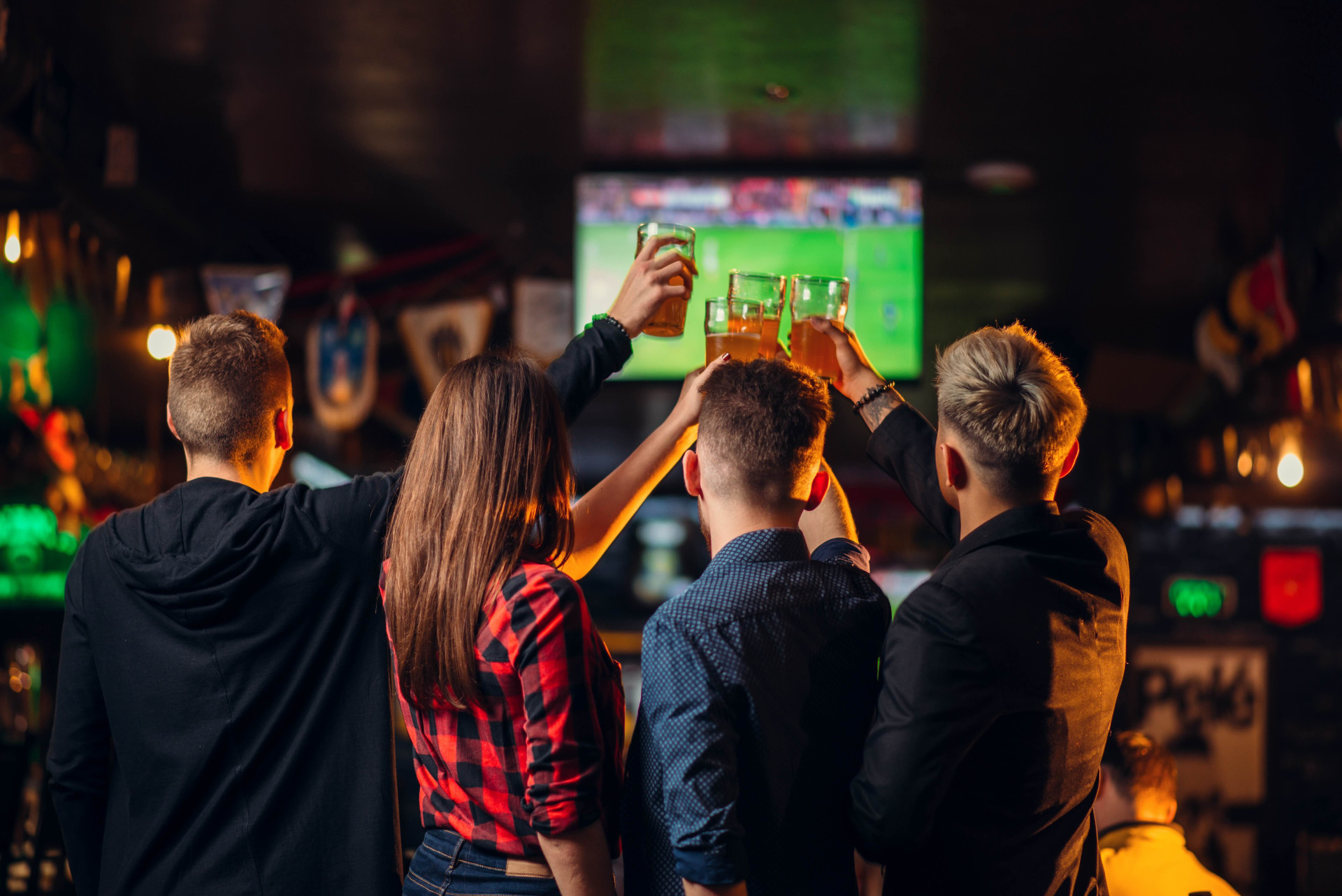 Friends toasting and watching football in a bar. Vänner skålar och ser på fotboll i en bar.