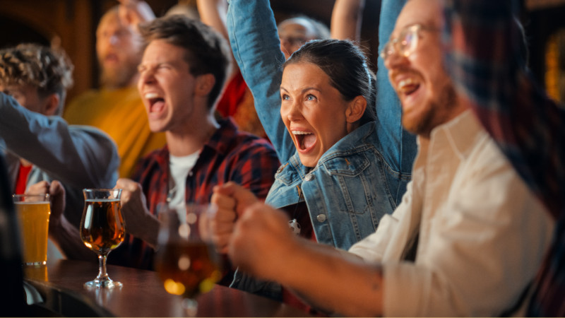 Friends cheering and watching sports in a bar. Vänner som jublar och ser på sport i en bar.