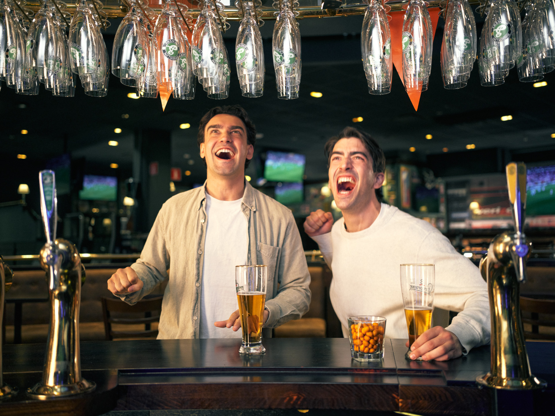 Två personer som hänger i en bar, dricker öl och tittar på sport.