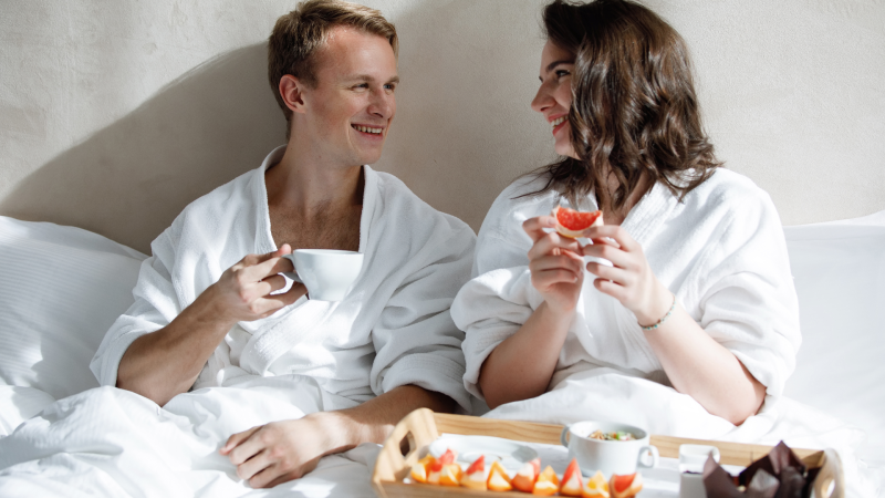 Ett par som äter frukost i en hotellsäng.