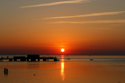 Sunset over the sea, people on a long pier. Solnedgång över havet, folk på en lång brygga.