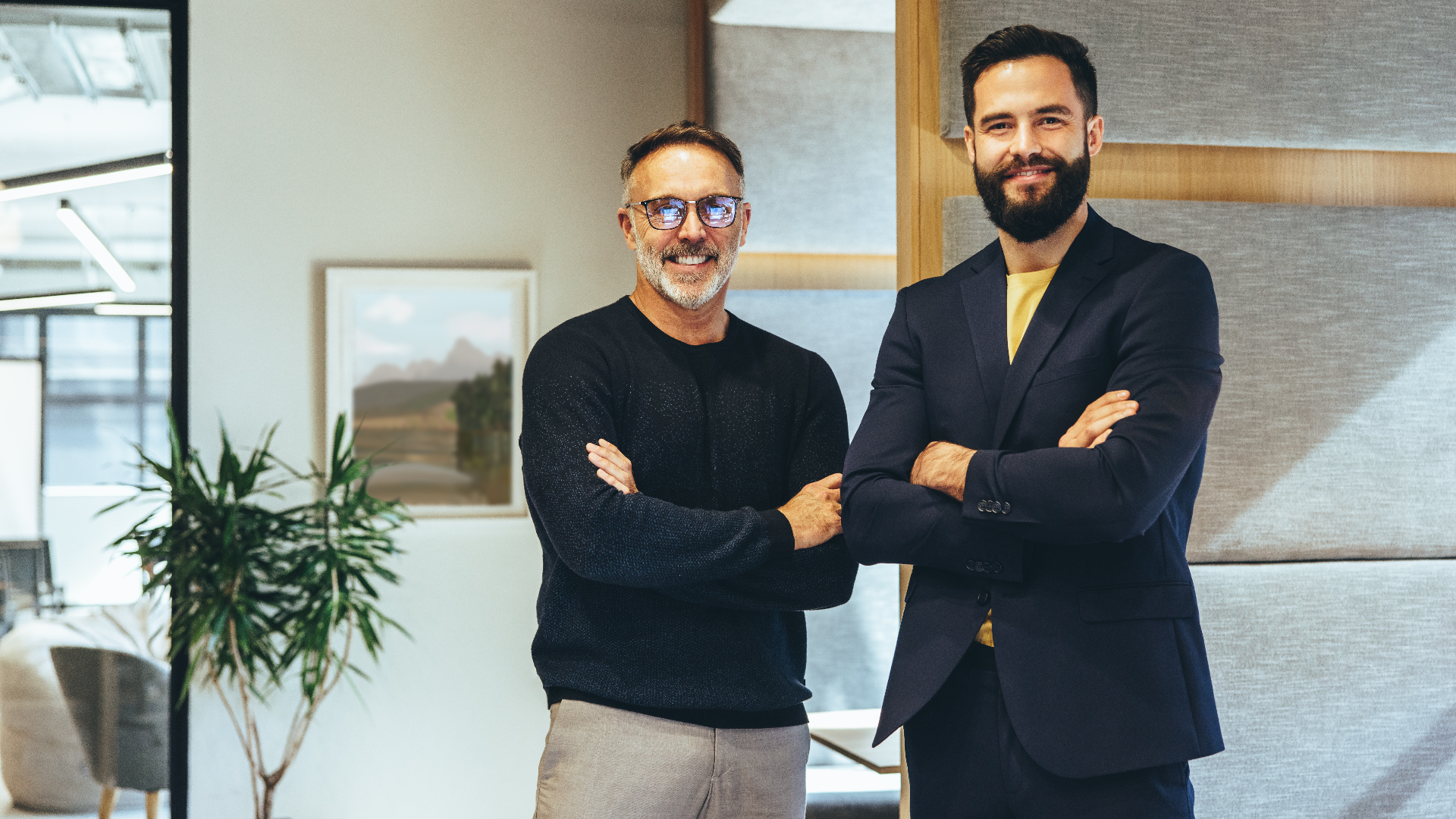 Two male project managers with their arms crossed in an office. Två manliga projektledare med armarna i kors på ett kontor.